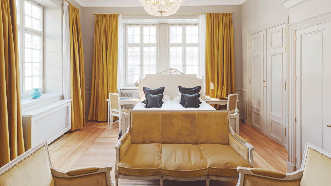 Stor King Superior rom med king size-seng, og sennepsgul sofa og gardiner.