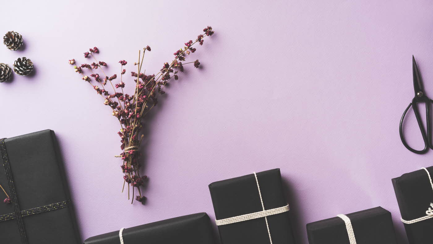 En rekke med svarte gaver og blomster på lilla bakgrunn