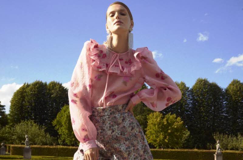 dame poser med rosa blomstrete bluse og shorts i park