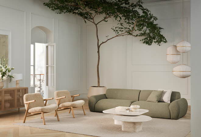 En stor stue med en grønn sofa og to lenestoler, med et tre i bakgrunnen