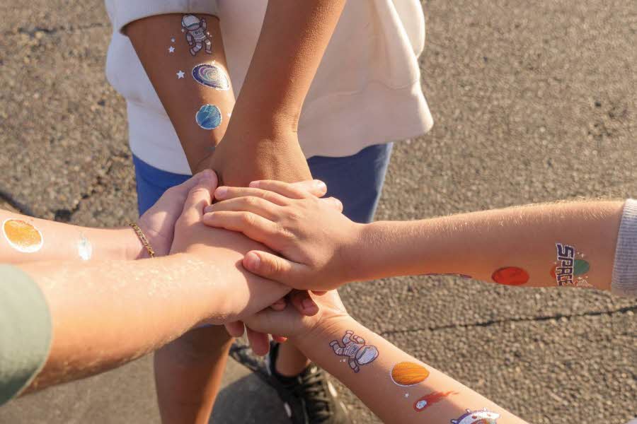 Små barn som holder hendene sine oppå hverandre med tatoveringer på armene