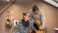 To ansatte i Global Ensemble Drama koser med en hund på kontoret 