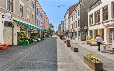 Handlegaten Torggata, sett fra øst til vest. Gågaten er pyntet med blomsterkasser og brostein. En grønnsakshandel på venstre side og restauranter med uteservering på høyre side.
