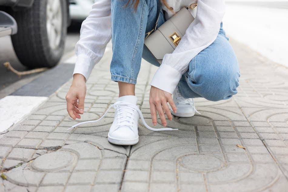 Nærbilde av damehender som knyter lisser på hvite sneakers på fortau