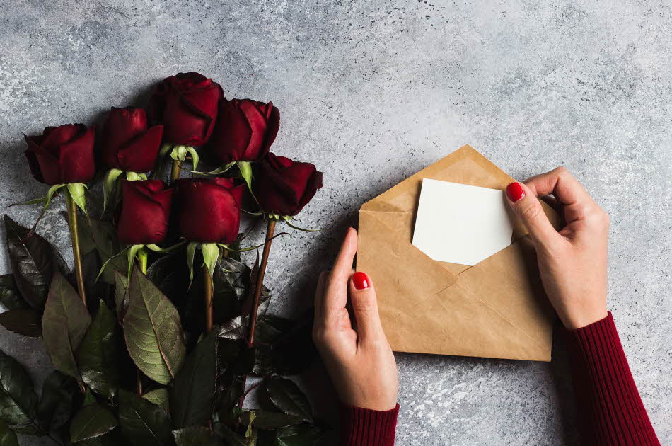 Dame åpner konvolutt ved siden av en bukett med roser