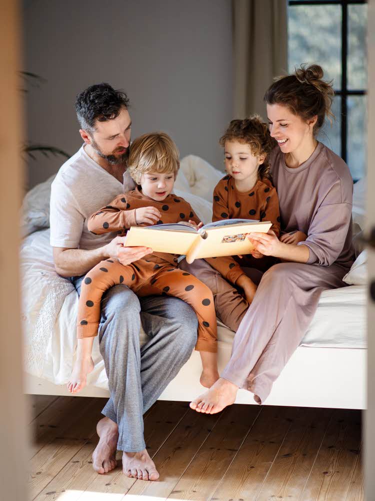 Mor, far og to barn i pyjamas som sitter på senga og ser gjennom et bilde album