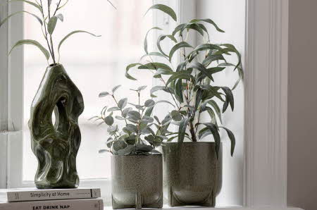 En grønn vase og to potter med planter stående på en vinduskarm