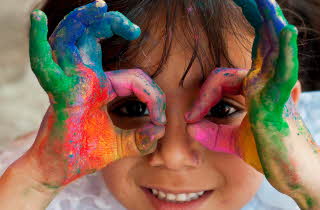 En jente med hendene dekket av flerfarget maling