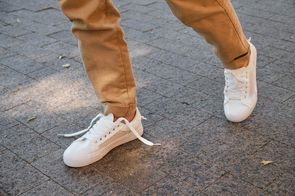 Manneben med brun bukse og hvite joggesko går på gata