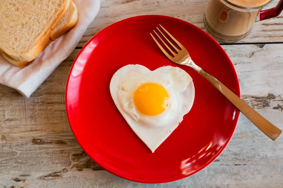 hjerteformet speilegg på rødt fat, sammen med en gaffel og med ristet brød og en lattekopp ved siden av