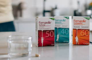 Tre pakker med forskjellig type Femarelle står på en kjøkkenbenk med et glass vann