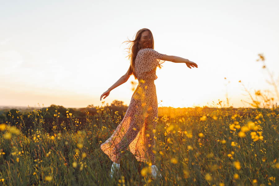 Dame med lang blomstrete kjole danser i gul blomstereng i vårsol 