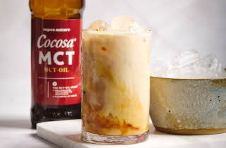 Et glass med iskaffe, en bolle med isbiter og en flaske med Cocosa MCT olje i bakgrunnen