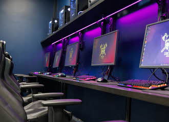 PC-skjermer på en rekke i et rom med lille LED-lys på veggen bak. Foto.