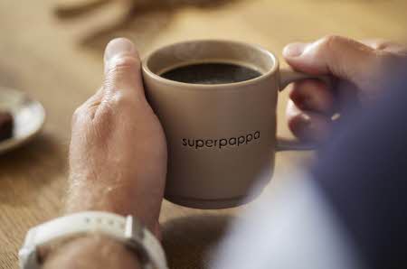 En mann som holder en kopp kaffe med tekst "superpappa" på koppen