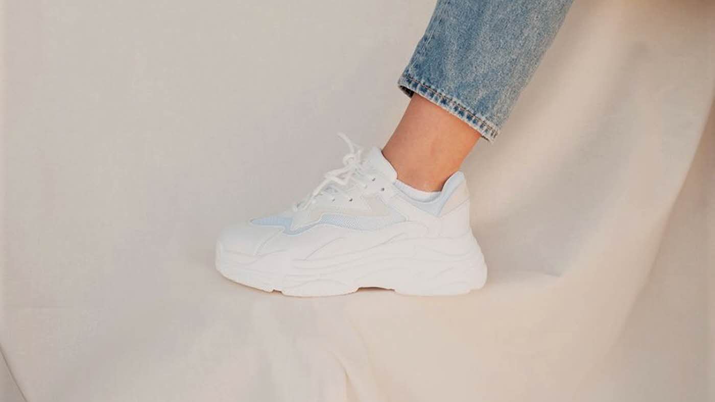 Hvit sneakers på fot med hvit bakgrunn