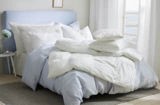 En seng på et soverom som redd opp, med et ekstra sett med dyne og pute oppe på sengen