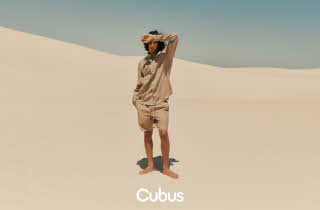 En mann i matchende linskjorte og -bukse står midt i en ørken
