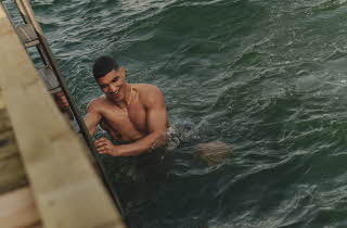 Bilde av en mann som er nede i vannet og holder seg fast i stigen på en brygge, mens han ler
