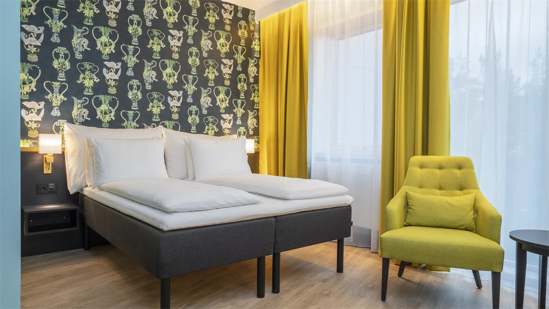 Mønstrete tapet med grønne detaljer, dobbeltseng, gule gardiner og gul stol i business rom på Thon Hotel Linne