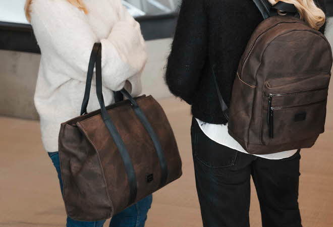 To kvinner står sammen, en med brun bag og en med brun sekk