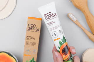 En hånd som holder en tube med Eco Denta tannkrem, ved siden av boksen den var i og en tannbørste