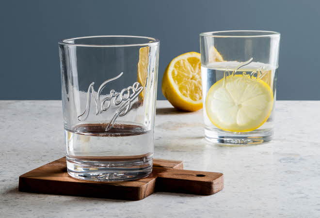 To Norgesglasset med vann, hvor den ene også inneholder en sitron.