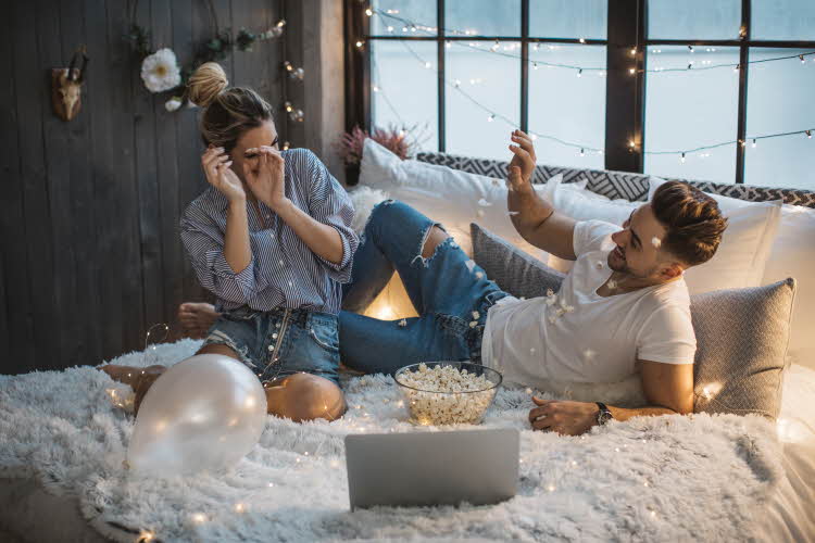 Kjærestepar ligger i sengen med pc og popcorn