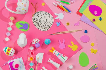 Kaninformer klippet ut i filt, malte gips egg, pensler, og diverse hobby saker mot en rosa bakgrunn