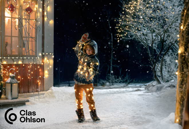En gutt som står surret i en lyslenke ute i snøen.