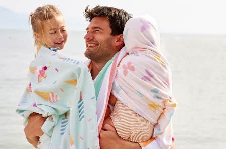 En mann som holder to barn som er pakket inn i hvert sitt strandhåndkle