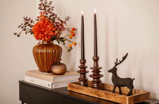 Et sidebord med blomster i vase, noen bøker, et fat med lysestaker og en figur av et reinsdyr