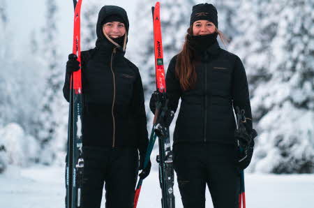 To kvinner holder langrennski og er kledd i sportslige vinterklær