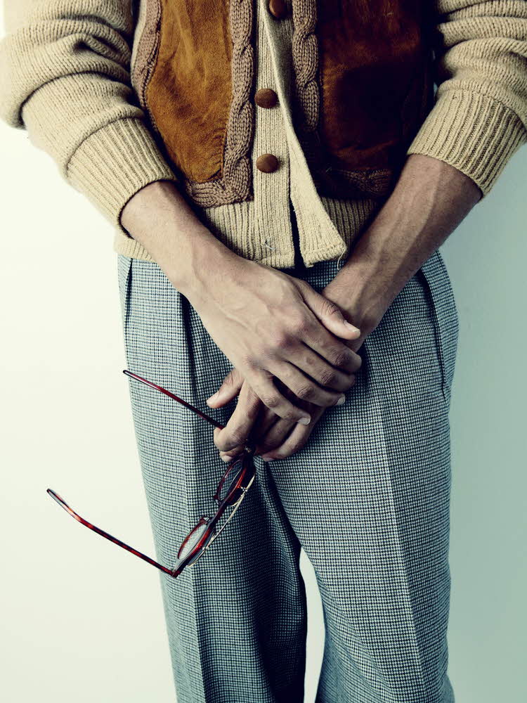 Nærbilde av mannehender som holder briller med rutete dressbukse og beige cardigan