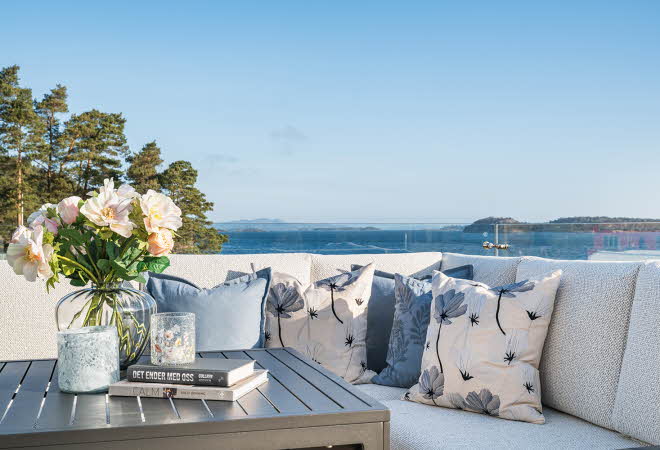 Utendørs sitteområde med utsikt over vannet og blomsterdekorasjoner.