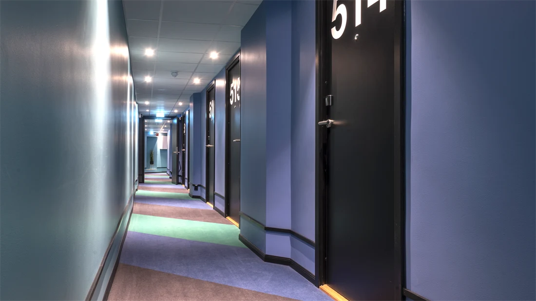 Korridor med fargerik bred stripete teppe, blå vegger og store hvit romnummer på sorte dører på Thon Hotel Astoria i Oslo 