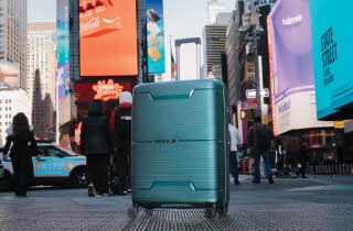 Turkis koffert med fire hjul på en gate i Times Square, New York.