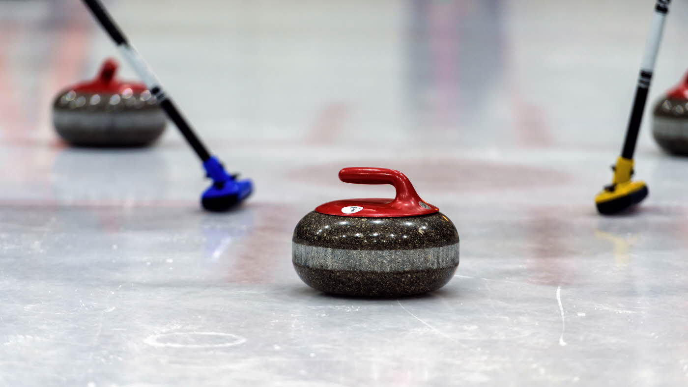 Curlingkule på vei med skaft i bakgrunnen