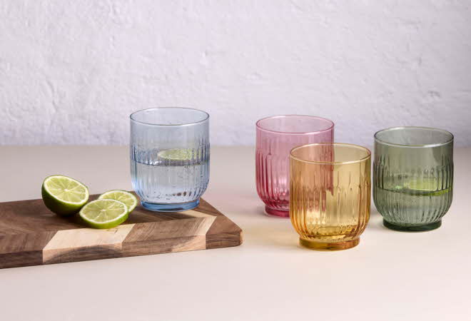 Fire fargede glass står ved siden av et skjærebrett med to limehalvdeler.