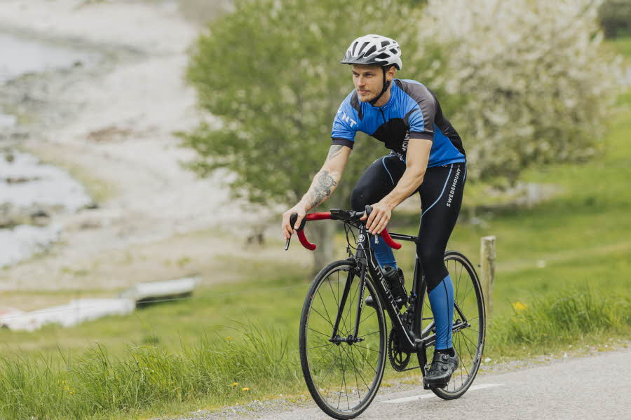 mann på sykkel med sølv sykkelhjelm, blå og sort t skjorte og tights