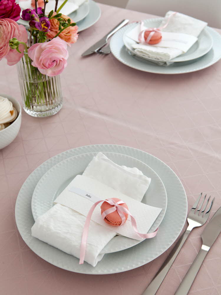 Steg fem - Bord dekket med tallerkener og hvit linservietter og en rosa makron og bestikk på en rosa duk  Steg 6 -  Bord dekket med tallerkener, hvit linservietter, farerike blomster på rosa makron på en rosa duk
