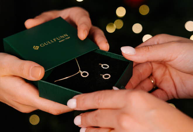 Nærbilde av et par hender som gir et annet par hender en boks med et smykkesett.