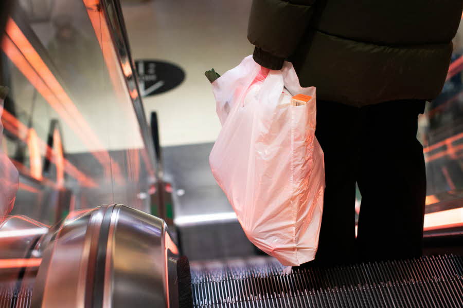 Person som står i rulletrapp og holder en plastpose