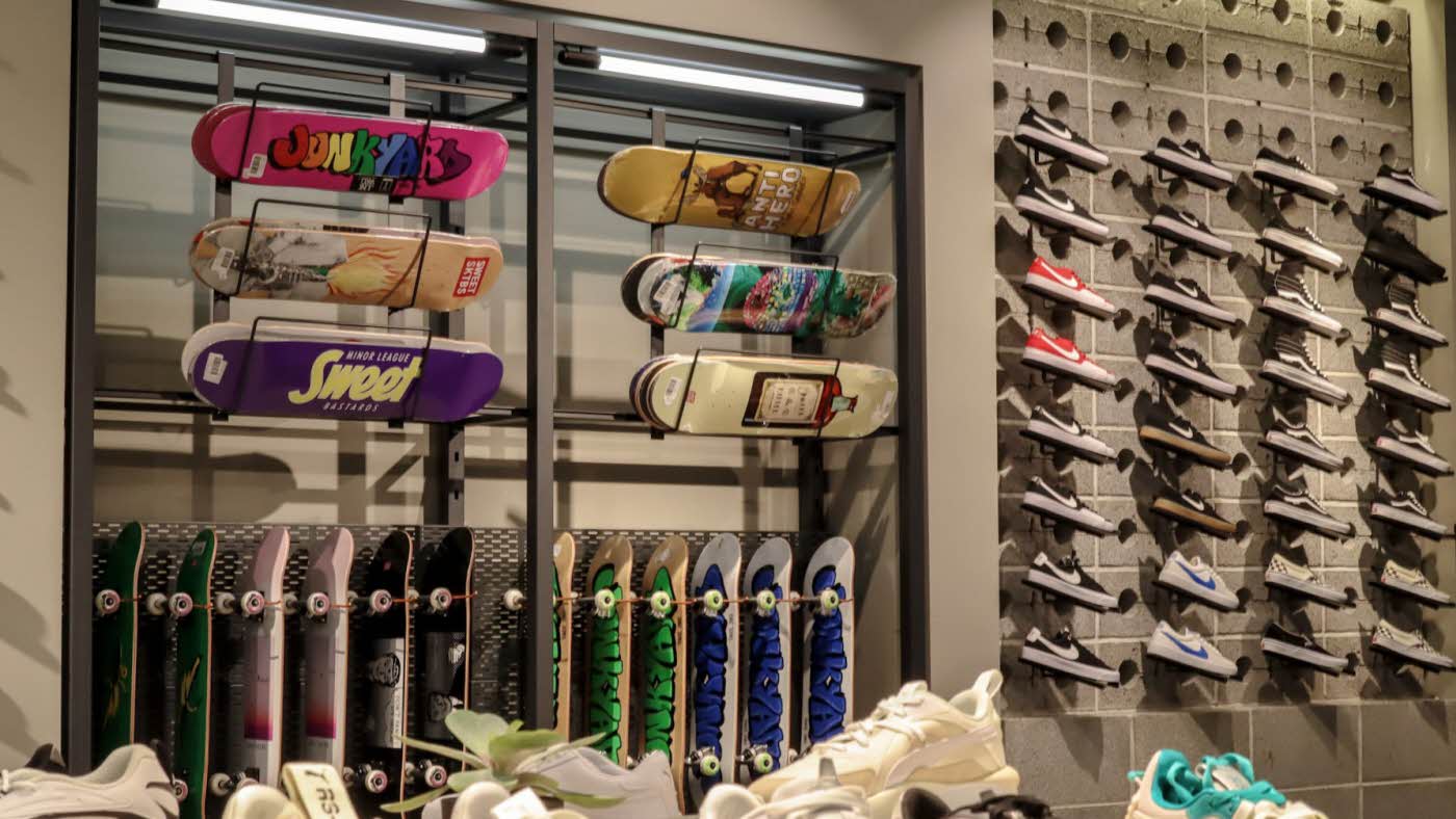 Lysskilt med tekst "Sneaker dept." og butikk i bakgrunn Nærbilde av stativ med skateboard Butikkfasade med lysskilt, logo til "Junkyard" Vegg med skateboard og sneakers på hyller