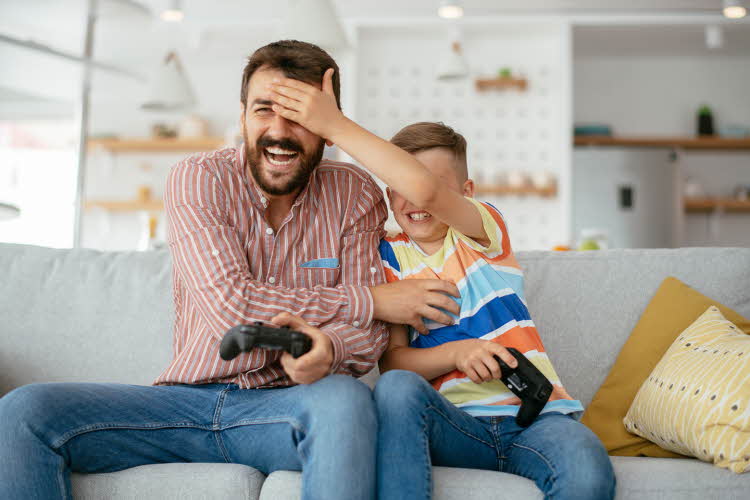 Gutt holder hånden foran øynene til mann mens de spiller tv-spill. Foto til artikkel om opplevelsesgaver til farsdag
