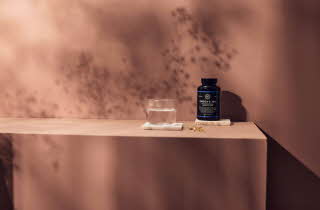 En flaske Omega-3 tilskudd, et glass vann og tre gule kapsler.