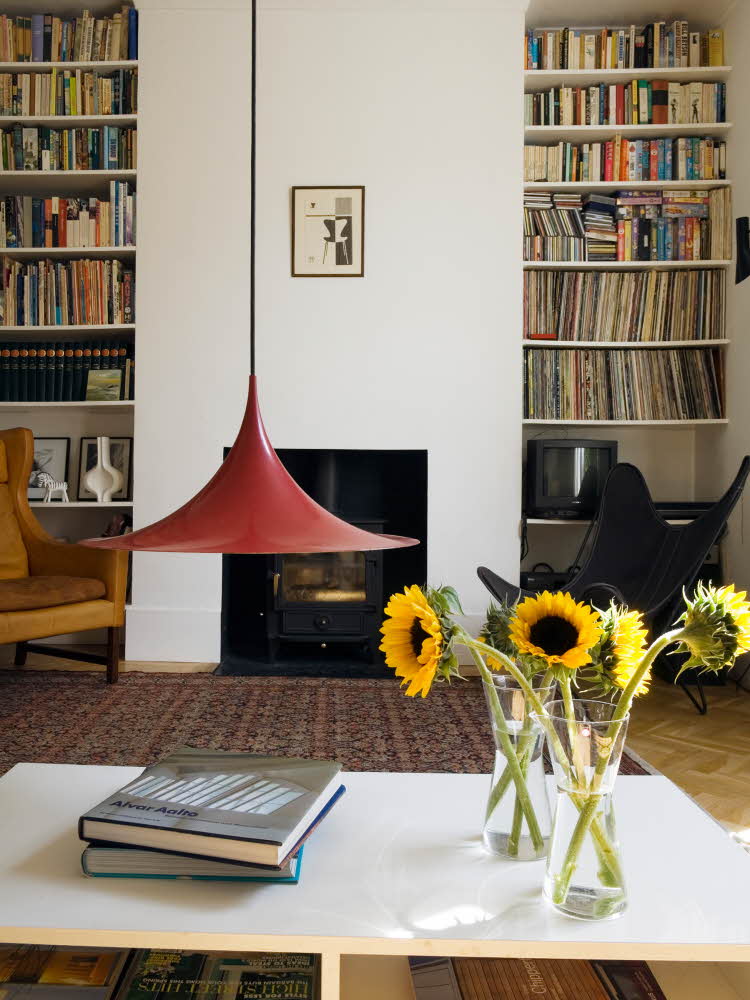 Stue med rød statementlampe, bord med gule solsikker og hyller med LP-plater og bøker i bakgrunnen