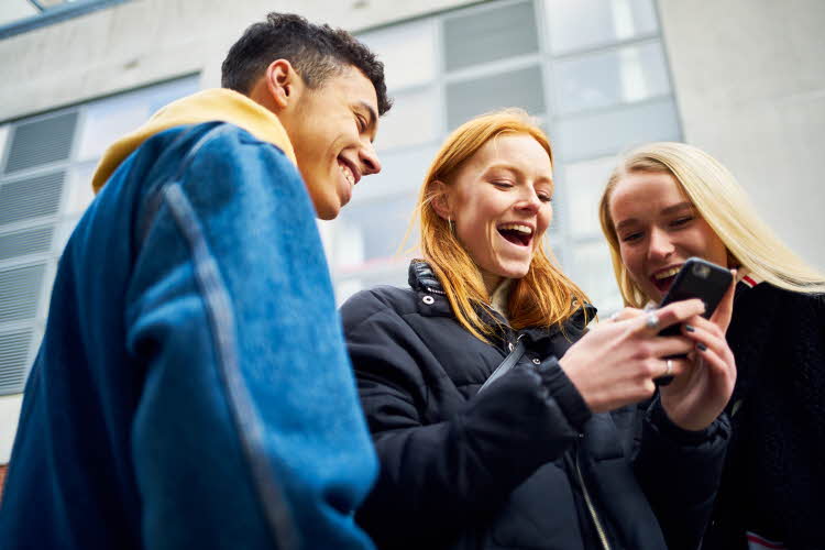 ungdommer som ser på telefon påkledd allværsjakke og denimjakke