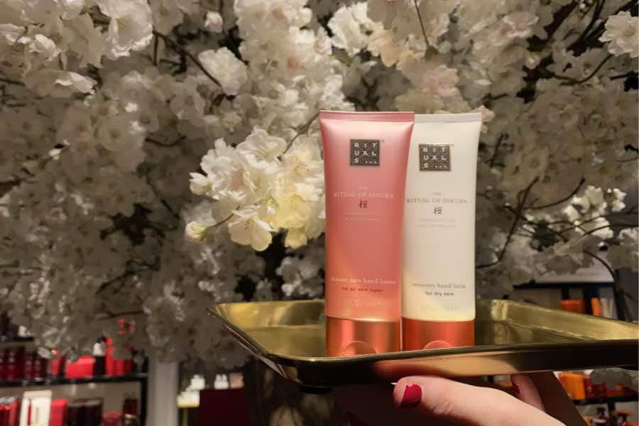 hudprodukter fra Rituals som står på et gullfat med hvite kirsebærblomster i bakgrunnen