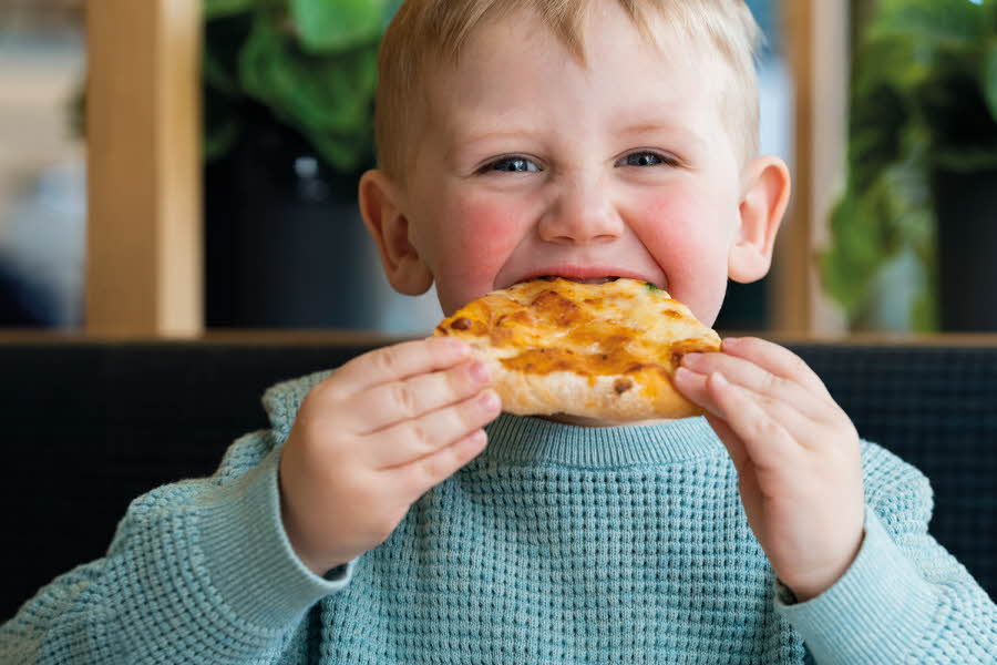 smilende-liten-gutt-med-lys-blå-genser-som-spiser-pizza